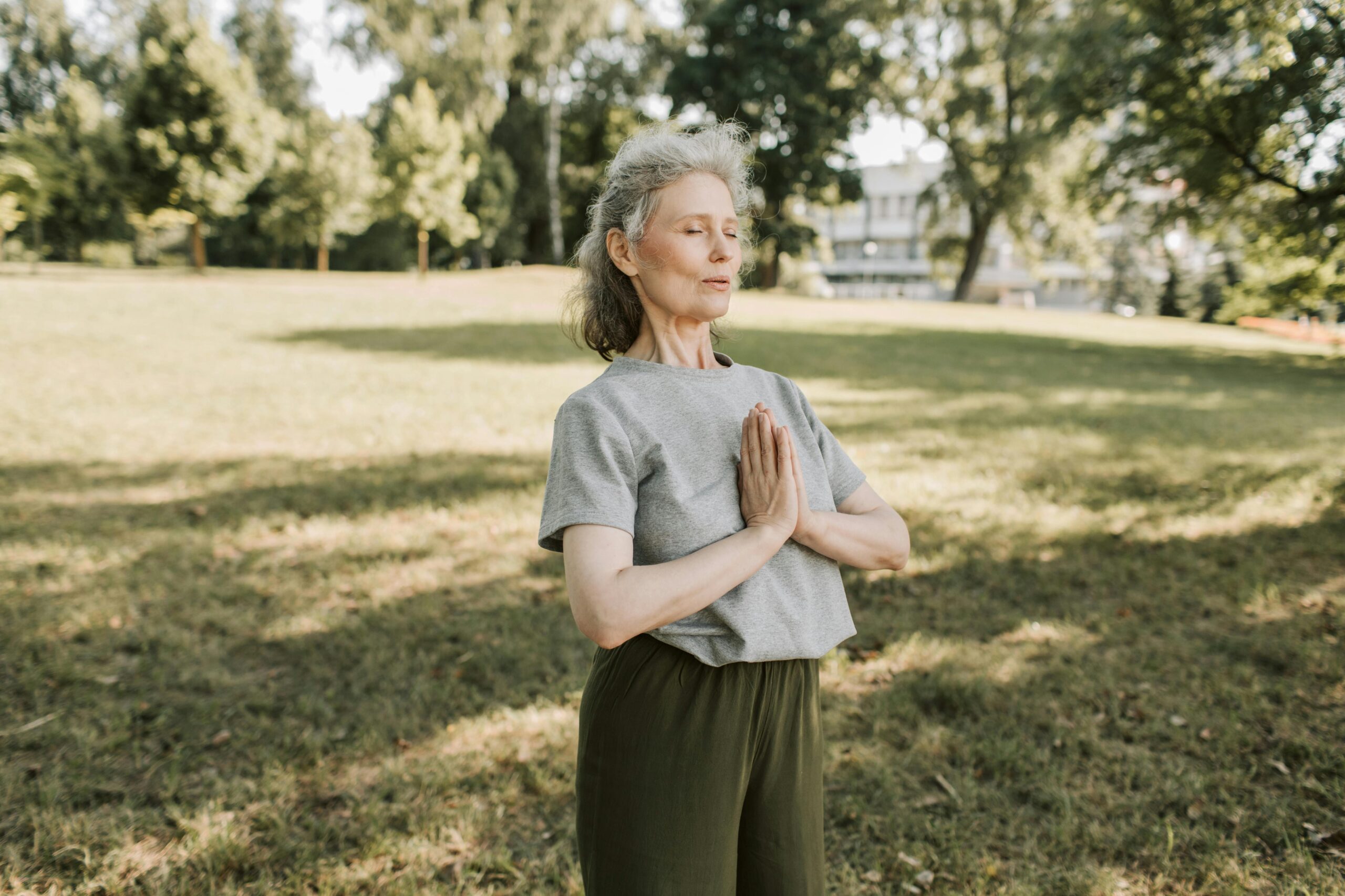 Elderly woman meditating and practicing yoga in a sunny park, embracing wellness and mindfulness.